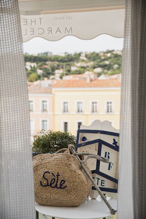 A view through a window with a wicker bag labeled "Sète" and a decorative sign with "MAROC LES SUITES" visible.