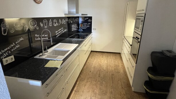 A modern kitchen with a black countertop, white cabinets, and a wooden floor.