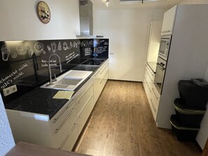 Een moderne keuken met een zwart aanrecht, een roestvrijstalen spoelbak en houten vloeren.