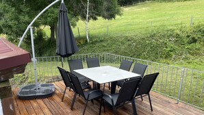 A wooden deck with a white table and black chairs, surrounded by a metal railing.