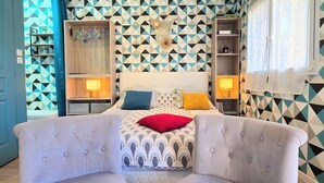 A bedroom with a geometric-patterned wall, a bed with multiple pillows, bedside tables with lamps, and a seating area with armchairs.