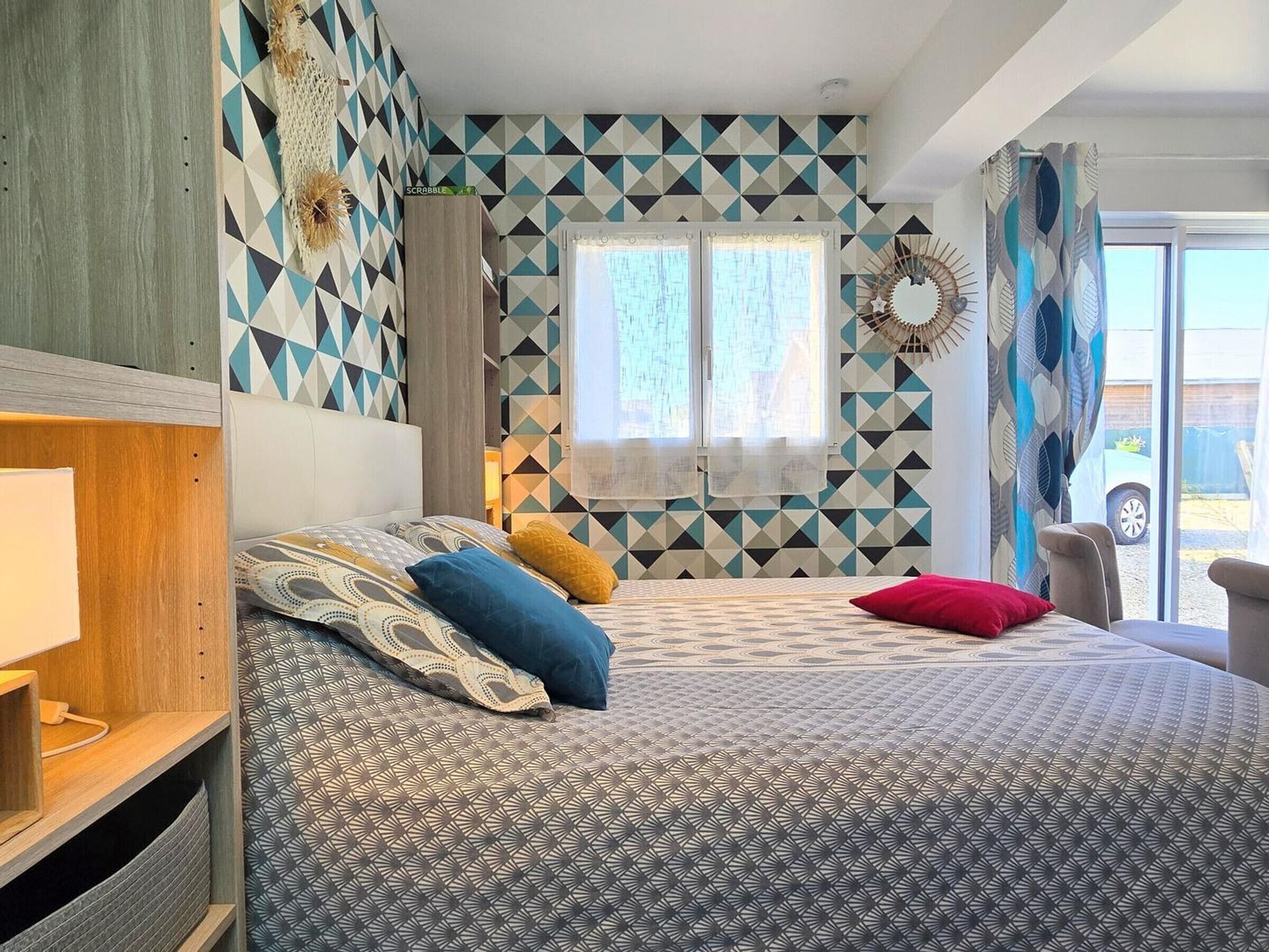 Een slaapkamer met een bed met een decoratieve spreidek, een hoofdbord, een nachtkastje en een raam met gordijnen.