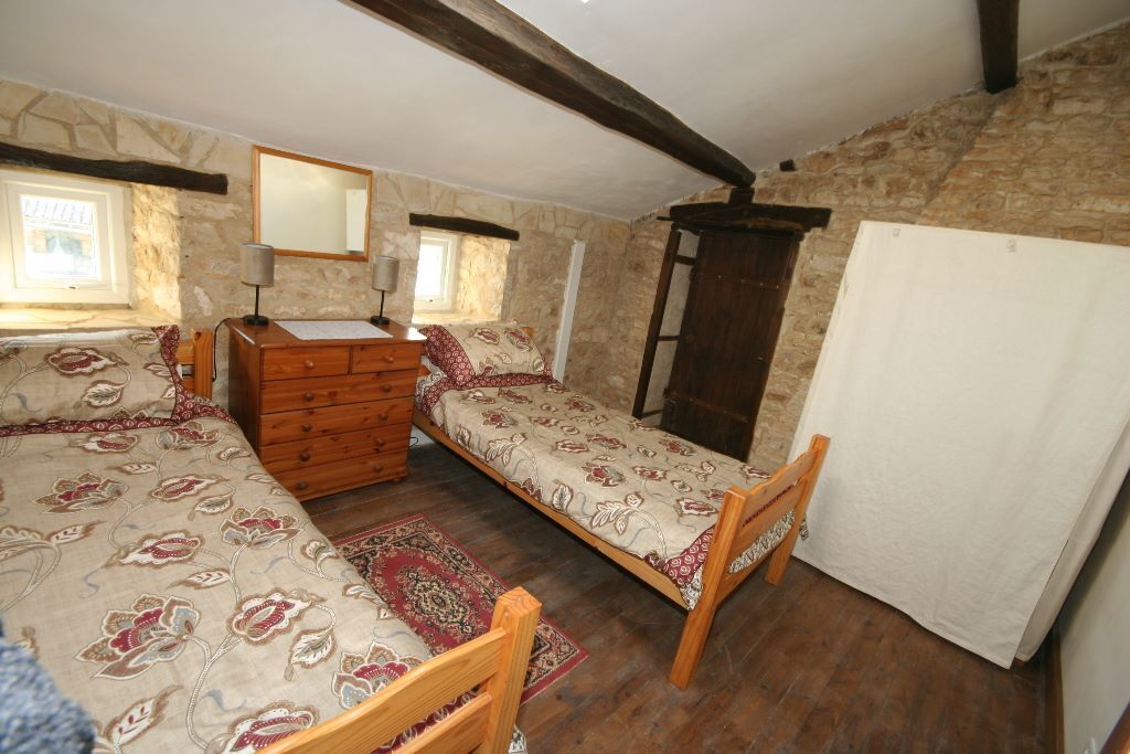 A bedroom with a wooden bed, a dresser, a mirror, and a stone wall.