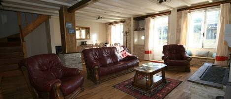 Un salón amplio con suelo de madera, chimenea de piedra y un ventanal grande con cortinas.