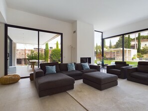A modern living room with a sectional sofa, a flat-screen TV, and a large sliding glass door leading to an outdoor patio. - Contemporary Villa with Pool Near Saint-Rémy Center, 4 Bedrooms, Garden (Saint-Rémy-de-Provence)