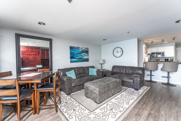 A modern living room with a glass dining table, leather sofas, and a kitchen area in the background. - GrandView 205 - Luxury Waterfront Condo (Chelan)