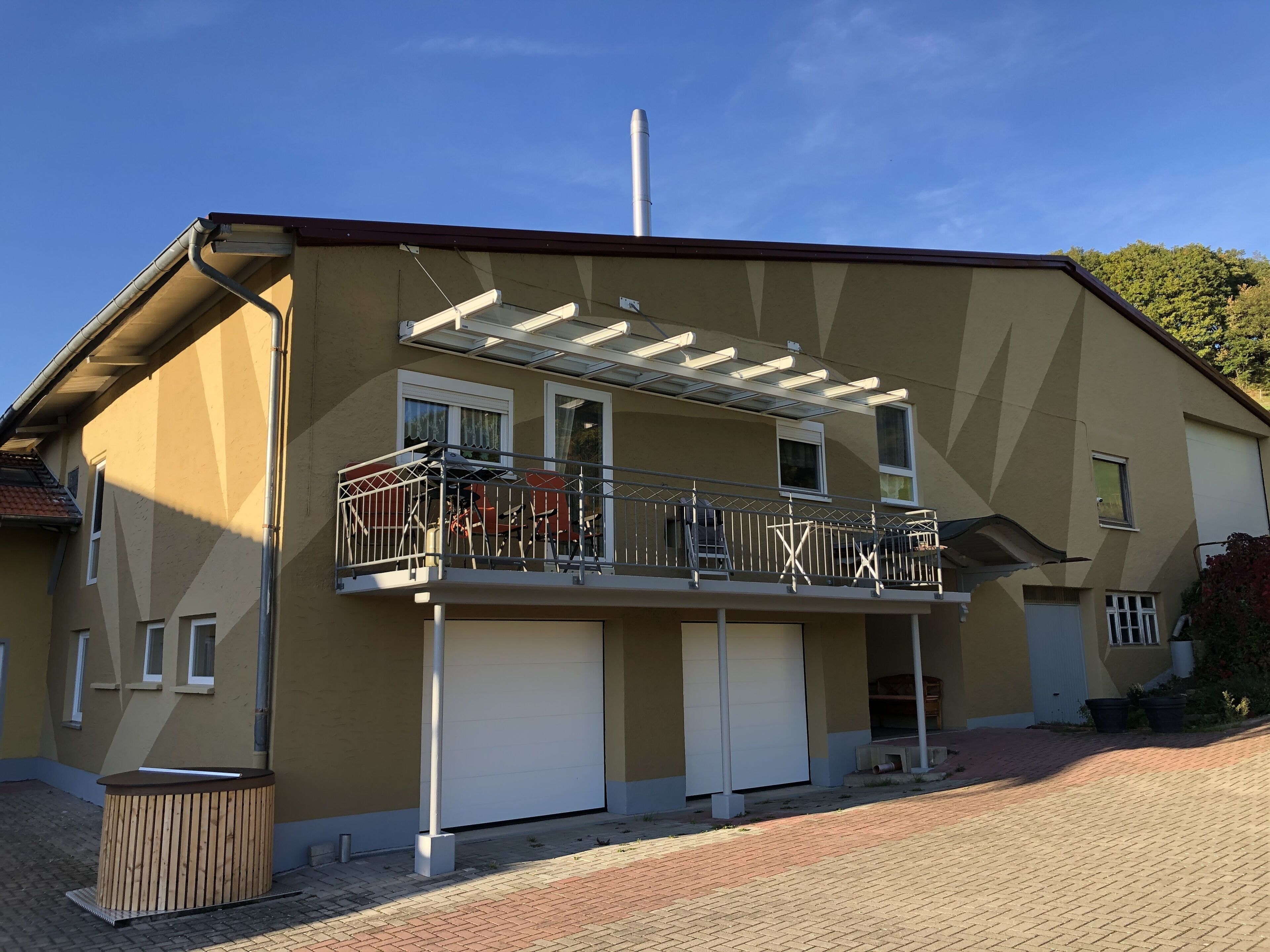 Ein zweistöckiges Gebäude mit Balkon, Garage und Schornstein.