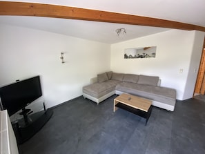 A living room with a sectional sofa, a coffee table, a flat-screen TV, and a ceiling light fixture.