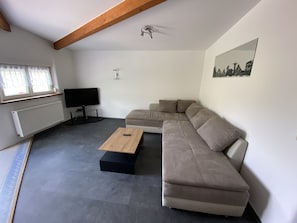 A modern living room with a sectional sofa, a flat-screen TV, a wooden coffee table, and a radiator.