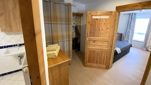 Un baño con lavamanos blanco, un mueble de madera y zona de ducha con cortina escocesa.