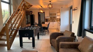 Una sala de estar moderna con una mesa de fútbol de mesa, un sofá de cuero marrón y una escalera de madera.