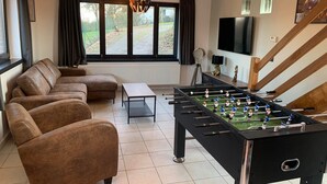 Una sala de estar con sofá, mesa de futbolín, mesa de centro, televisor y ventana con cortinas.