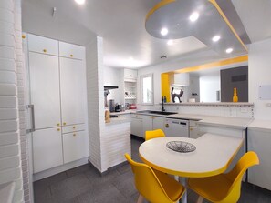 A modern kitchen with white cabinetry, a central island, and yellow chairs. - Villa d'Elsa 10-12 persons - heated pool - 500 m from the city center (sarlat la caneda)