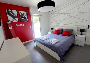A modern bedroom with a bed, nightstands, and a red accent wall.