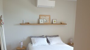 Ett sovrum med en säng, ett sängbord, en lampa, en väggmonterad luftkonditioneringsanläggning och en takfläkt.