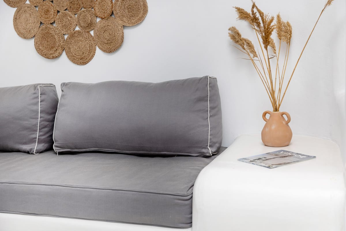 A modern living room with a grey sofa, a vase with dried plants, and a wall art piece.