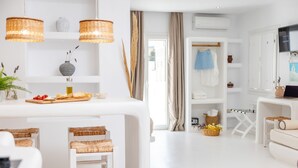 A modern, well-lit room with white furniture, wicker chairs, a dining area with a wooden board, and a TV on a stand. - Krina Mare (Naxos)