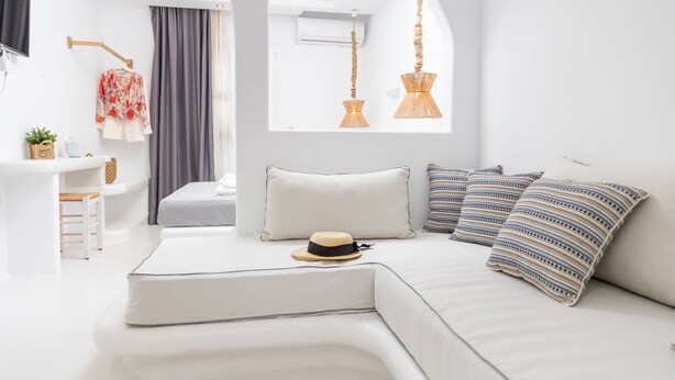A modern, white-themed bedroom with a curved sofa, a hat, and striped pillows. - Krina Mare (Naxos)