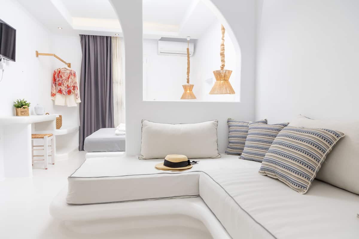 A modern, white-themed bedroom with a curved sofa, a hat, and striped pillows.