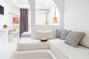A modern, white-themed bedroom with a curved sofa, a hat, and striped pillows. - Krina Mare (Naxos)