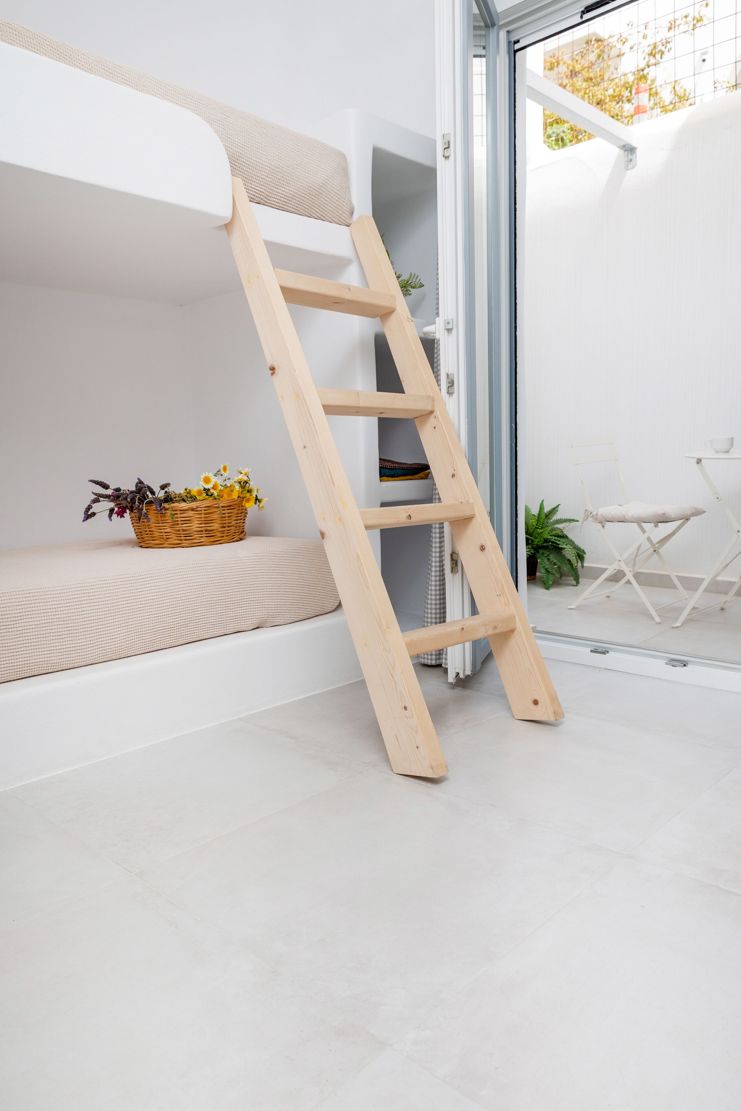 A bunk bed with a wooden ladder, a wicker basket with flowers, and a small table with a chair.