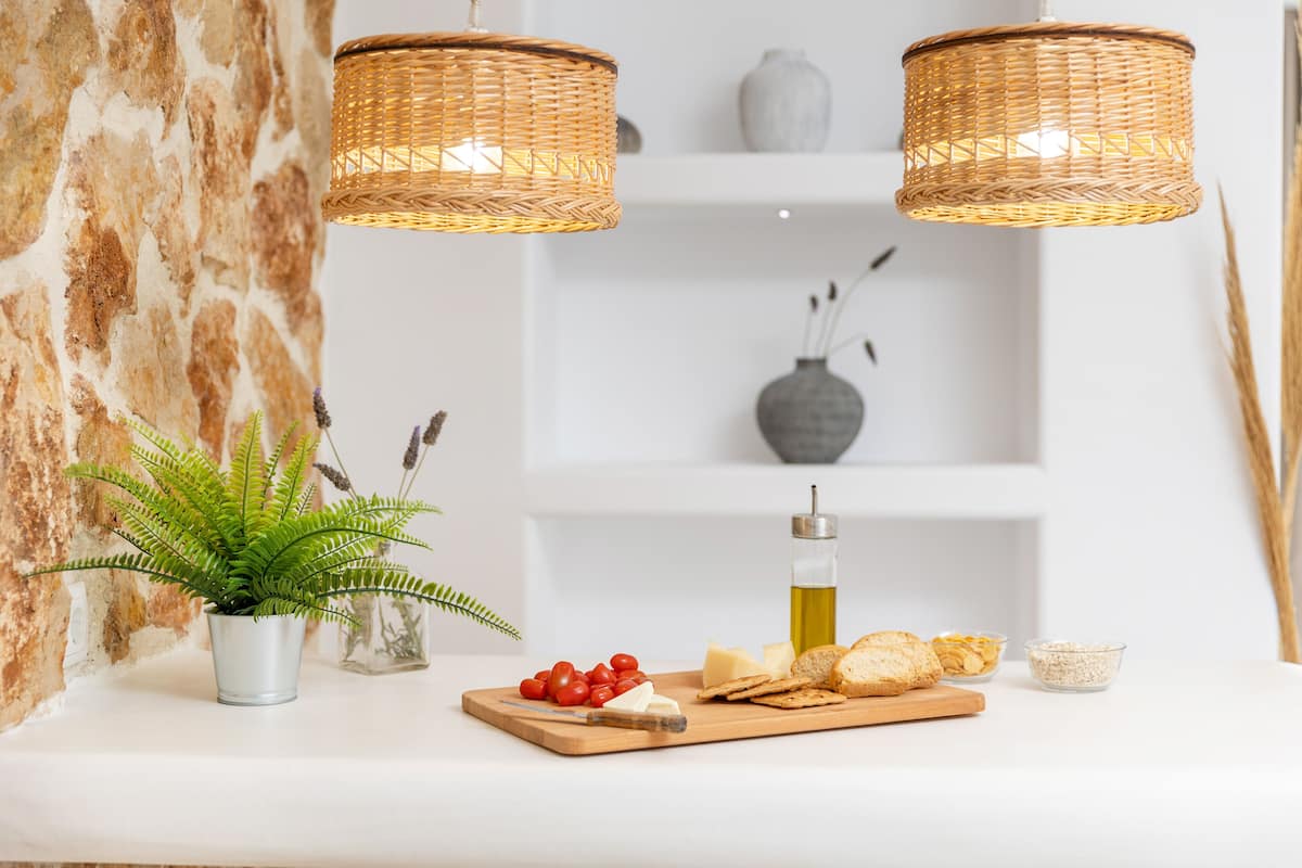 A kitchen counter with a cutting board, cheese, tomatoes, bread, and a bottle of oil.
