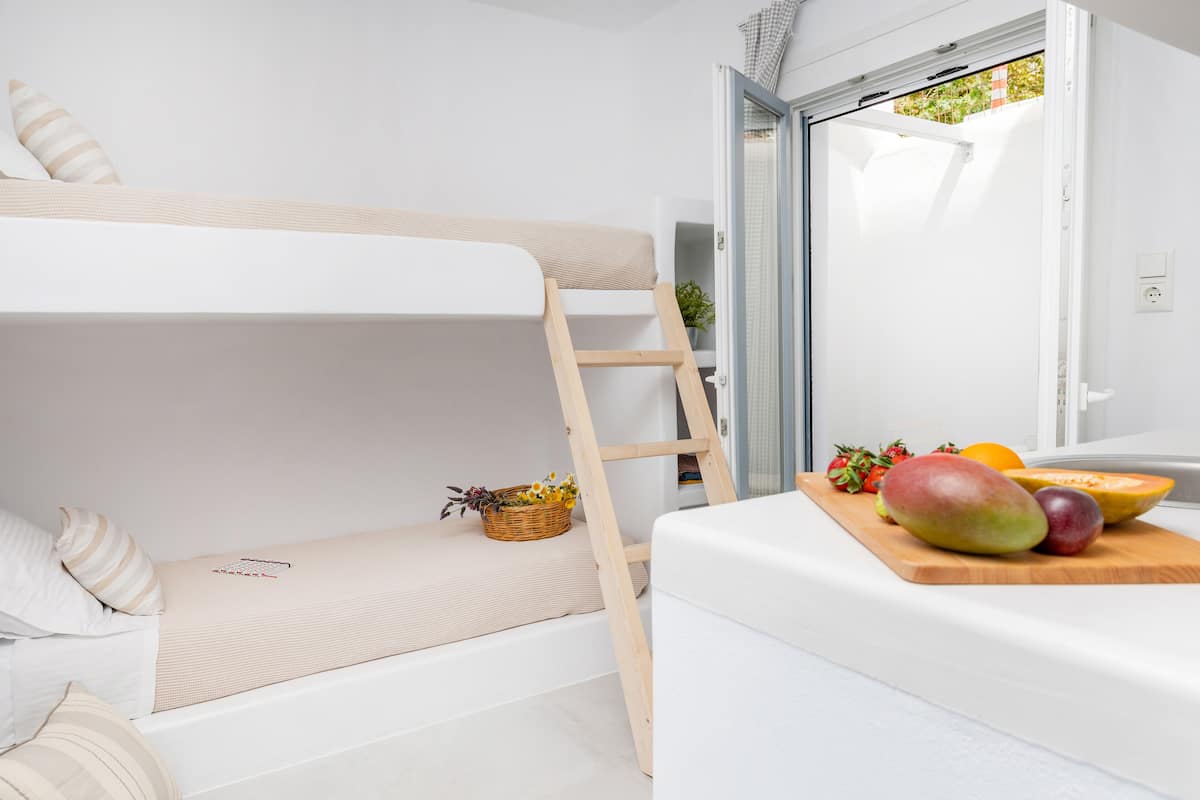 A bunk bed with a wooden ladder, a bedside table with a basket of flowers, and a fruit cutting board.