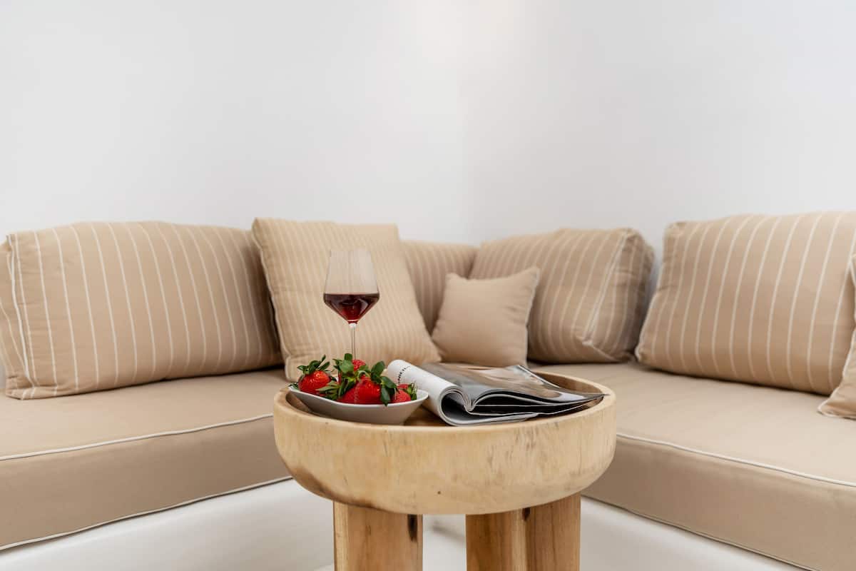 A sofa with striped cushions, a wooden side table with a bowl of strawberries and a glass of red wine, and a magazine.