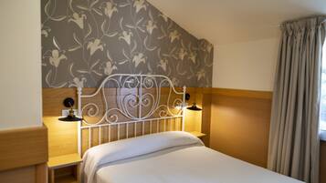A neatly made bed with a headboard, a bedside table with a lamp, and a floral-patterned wall.