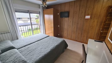 A bedroom with a bed, a ceiling fan, a TV, and a view of the outside balcony.