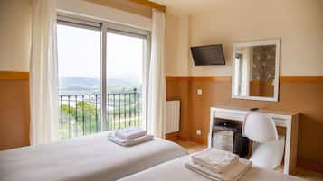 A hotel room with two beds, a TV, a desk, and a view of the outdoors.