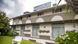 A hotel with a sign reading "HOTEL RÍA DE SUANCES". It features a brick facade, multiple windows with awnings, and flower boxes on the windowsills. - Hotel Ría de Suances (Suances)