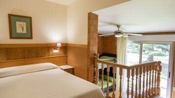 Habitación de hotel con una cama grande, cabecera de madera, mesita de noche, un cuadro enmarcado en la pared y un balcón con vistas al exterior.
