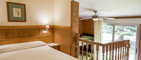 Habitació d'hotel amb un llit gran, un panell de capçalera de fusta, una tauleta de nit, un quadre amb marc a la paret i un balcó amb vista a l'exterior.