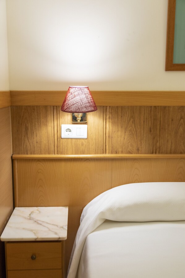 Una habitación de hotel con cabecera de madera, una mesita de noche con encimera de mármol y una lámpara roja.