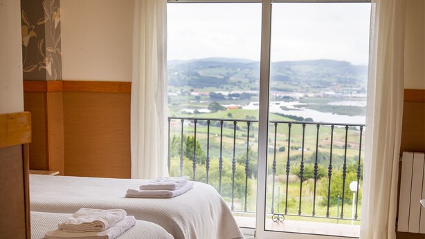 Habitación de hotel con cama, vista a un paisaje desde un balcón y ventana con cortinas.