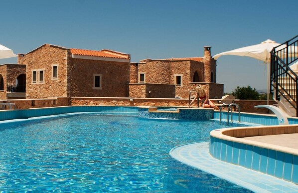 A swimming pool with stone buildings in the background. - Stone villa common pool (Παλαιλώνι)