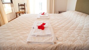 Ein ordentlich bezogenes Bett mit gefalteten Handtüchern und einer roten Rose, ein Holzstuhl und ein Fenster mit Vorhängen.