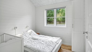 Une chambre avec un lit simple, une fenêtre donnant sur un espace verdoyant et une porte blanche.