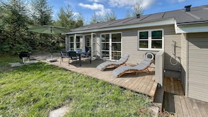 Une maison avec une terrasse, un espace salon extérieur et un barbecue.