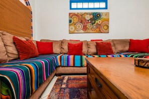 Un salon chaleureux avec un canapé d’angle, des couvertures colorées et une table basse en bois.