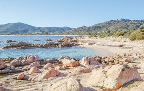 Une plage rocheuse bordée d’une eau d’un bleu limpide et dominée par des montagnes lointaines.