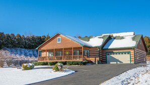 A log cabin with a porch, a garage, and a snow-covered landscape. - Log Cabin in West Jefferson - Fishing Pong + Hot Tub + Fire Pit + Mountain Views (West Jefferson)