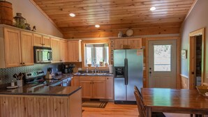 A kitchen with wooden cabinets, a stainless steel refrigerator, a microwave, and a stove. - Log Cabin in West Jefferson - Fishing Pong + Hot Tub + Fire Pit + Mountain Views (West Jefferson)