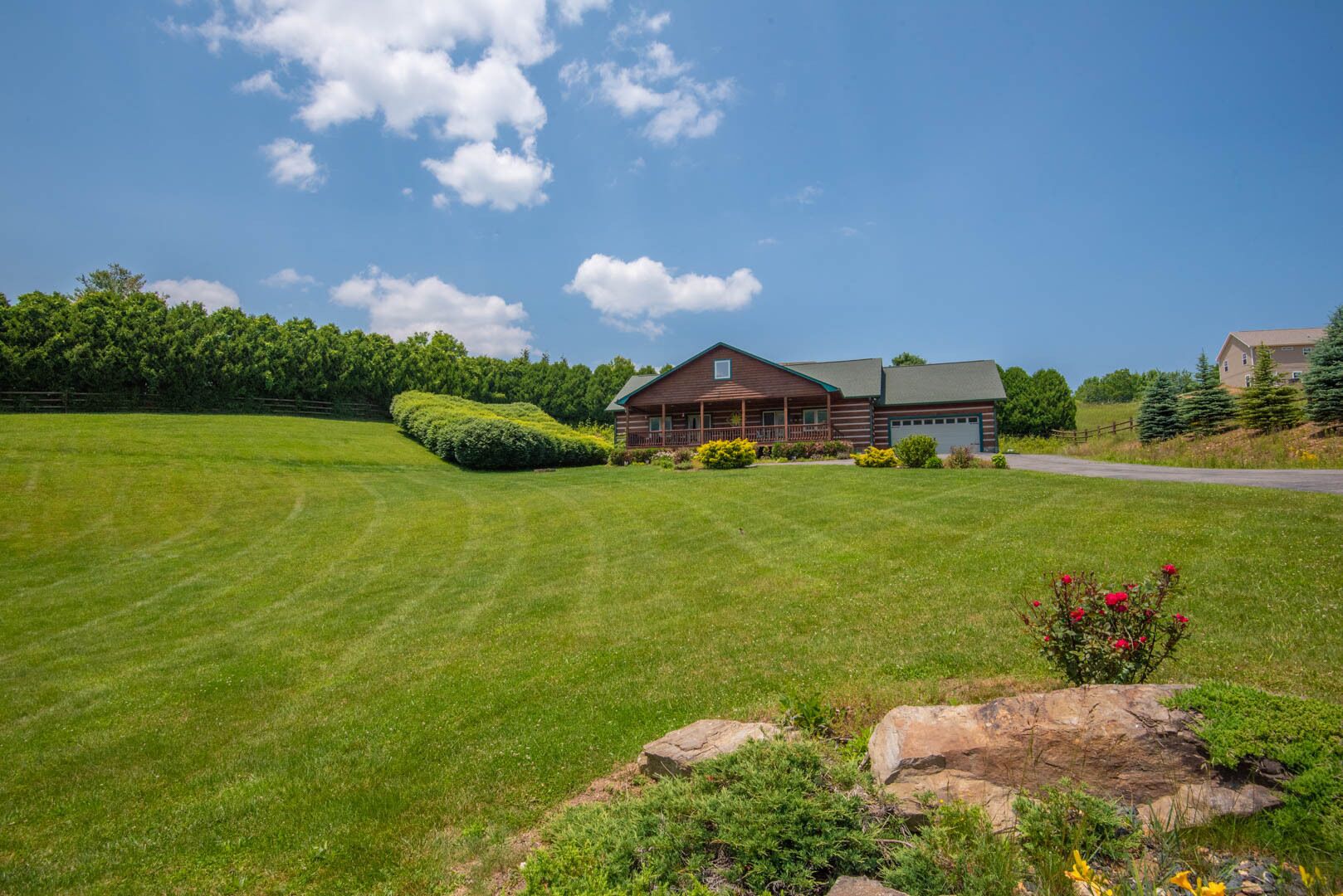 A large, well-maintained lawn with a wooden cabin-style house featuring a porch and garage.