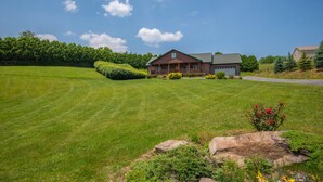 A large, well-maintained lawn with a wooden cabin-style house featuring a porch and garage. - Log Cabin in West Jefferson - Fishing Pong + Hot Tub + Fire Pit + Mountain Views (West Jefferson)