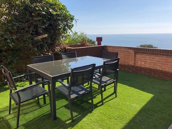 A patio with a glass table and chairs, a brick wall, and a view of the sea.