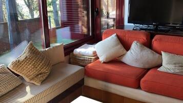 Un soggiorno con un divano rosso, una televisione e un'ampia finestra con tende.
