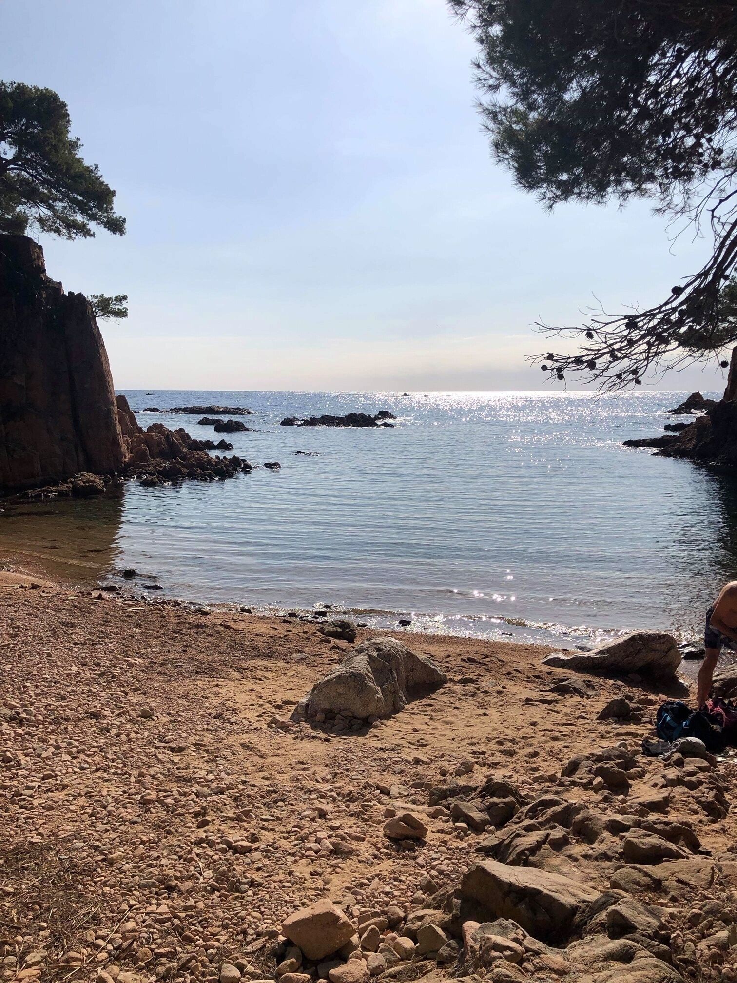 Una spiaggia rocciosa con acque cristalline e imbarcazioni all'orizzonte.