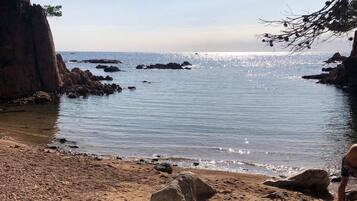 Una spiaggia rocciosa con acque cristalline e imbarcazioni all'orizzonte.
